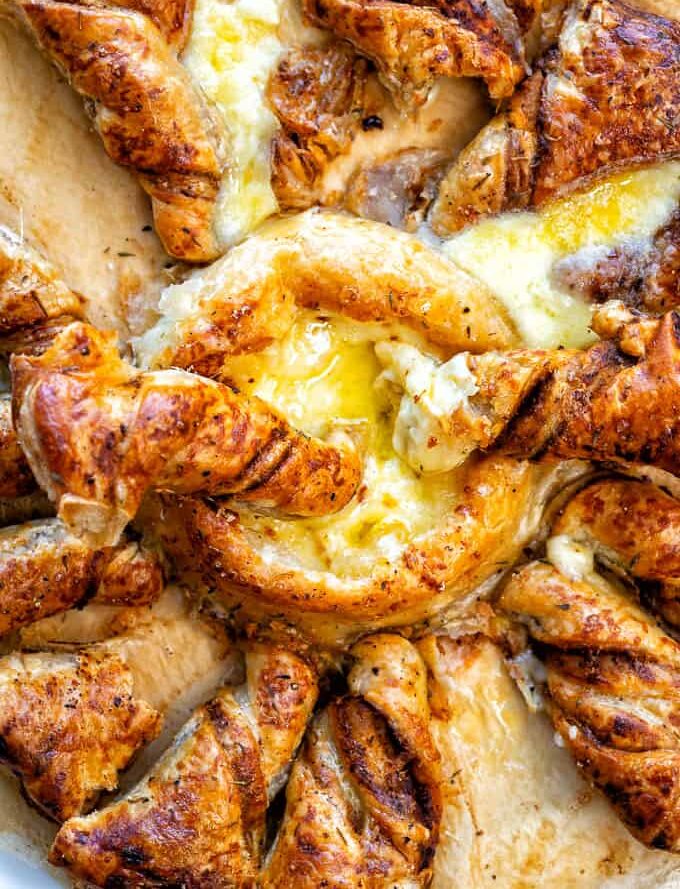 Golden, flaky baked brie puff pastry twisted into a star shape, filled with gooey melted cheese in the center and between the layers, resting on a sheet of parchment paper.