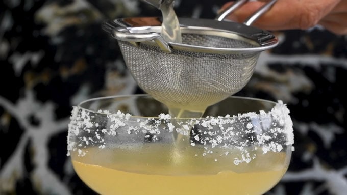 Close up of double straining a Grand Margarita into a frosted coupe glass