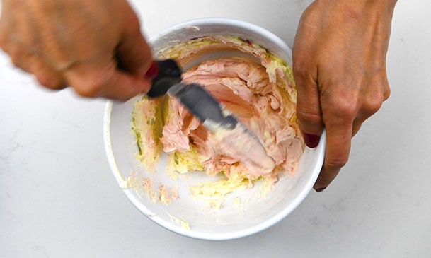 Tinting buttercream pink in a small bowl using offset spatula