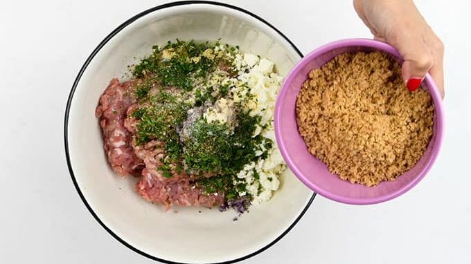 Adding ingredients for keftedes into a large bowl