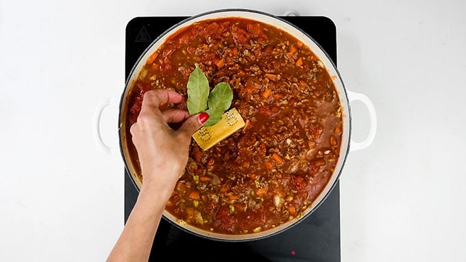 Adding parmesan cheese rind and bay leaves to bolognese sauce in a pan