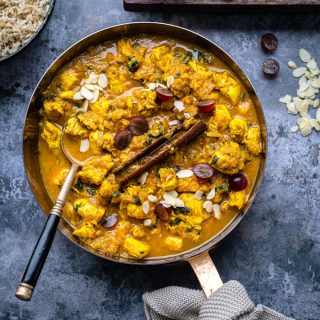 Pan of Chicken Korma garnished with grapes and flaked almonds on a rustic background