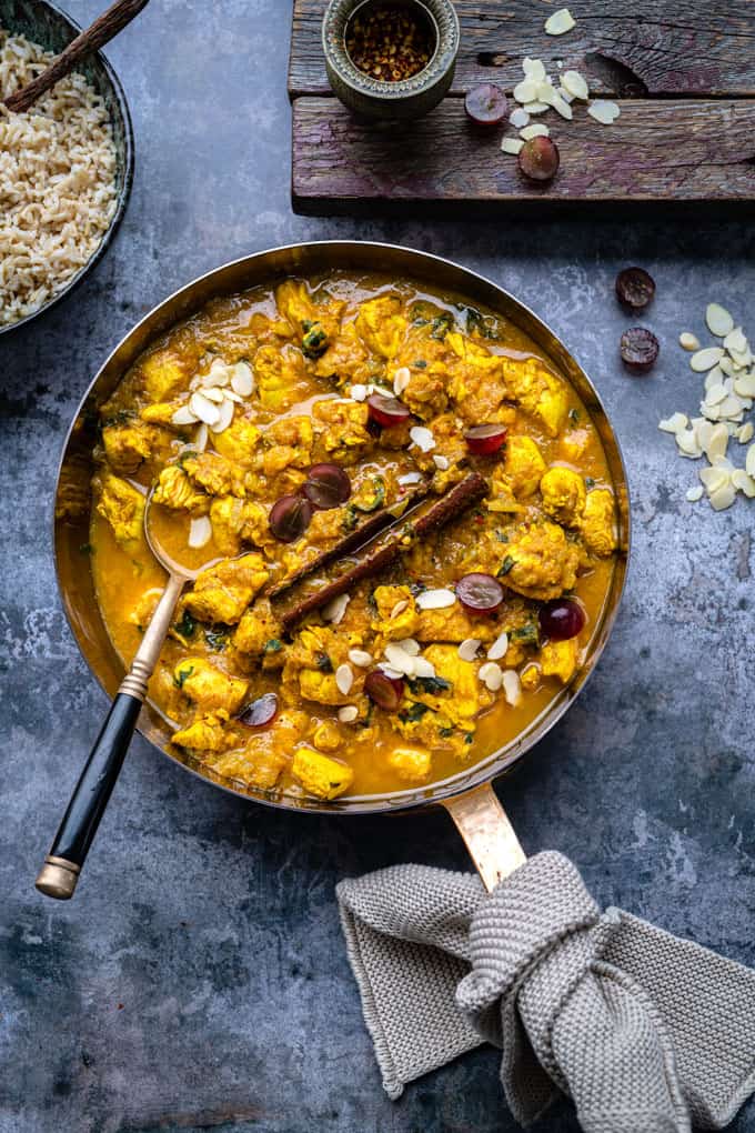 Pan of Chicken Korma garnished with grapes and flaked almonds on a rustic background
