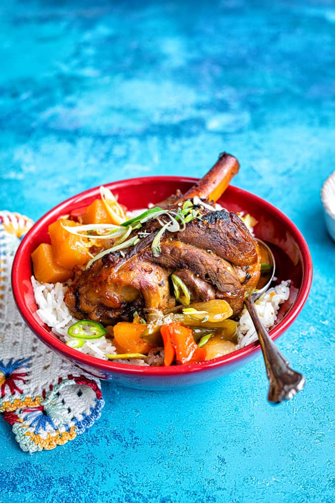Braised lamb shanks served with coconut rice in a red bowl