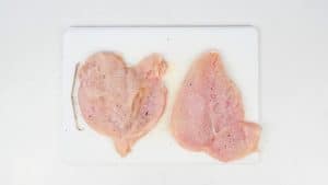 Butterflied chicken breasts seasoned with salt and pepper on a cutting board
