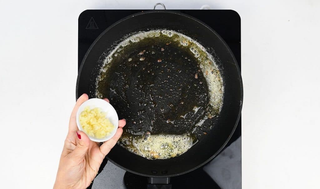adding minced garlic to a skillet of foaming butter