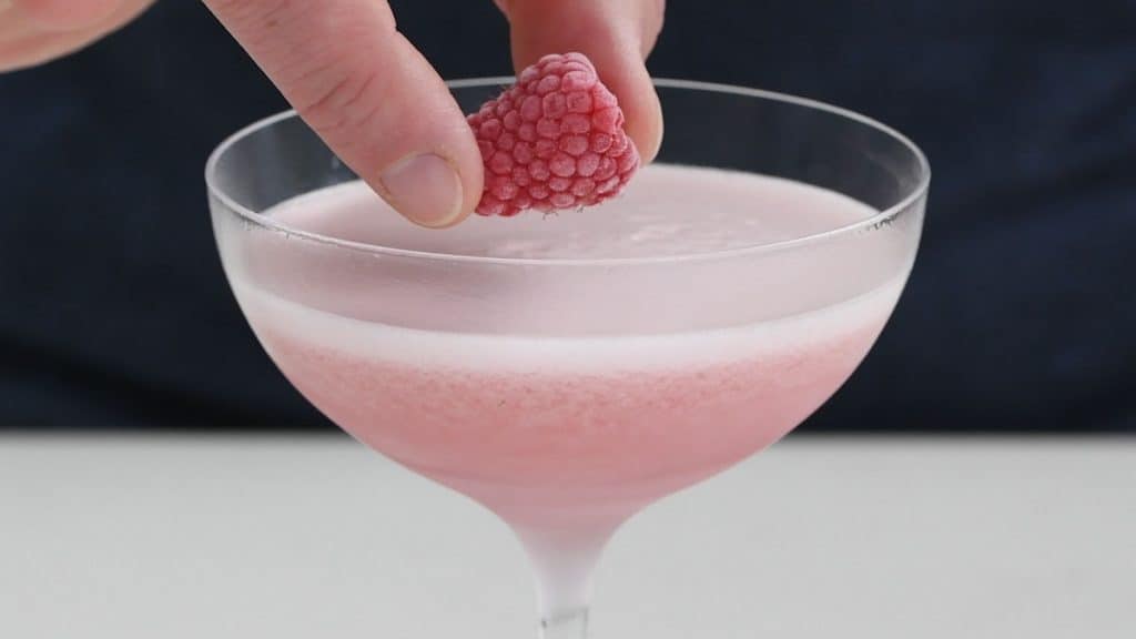 Frothy French Martini being garnished with a raspberry