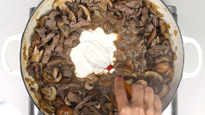 stirring sour cream into a stroganoff casserole
