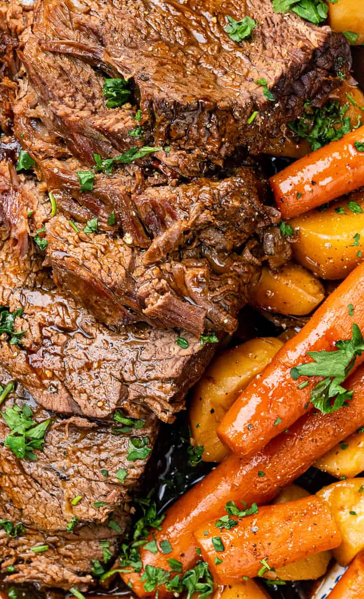 Close up on slow cooker roast beef sliced and served with gravy and vegetables