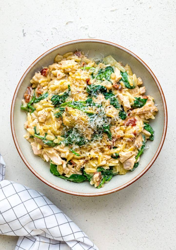 Bowl of Tuscan Orzo with turkey, spinach, sundried tomatoes with grated Parmesan garnish