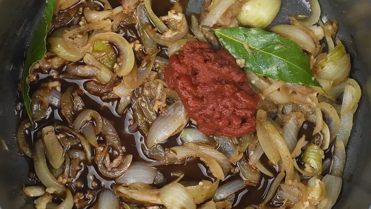 Close up of caramelised onions in a pot with tomato paste and bay leaves