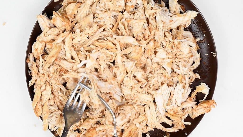 chicken breasts on a plate being shredded with two forks