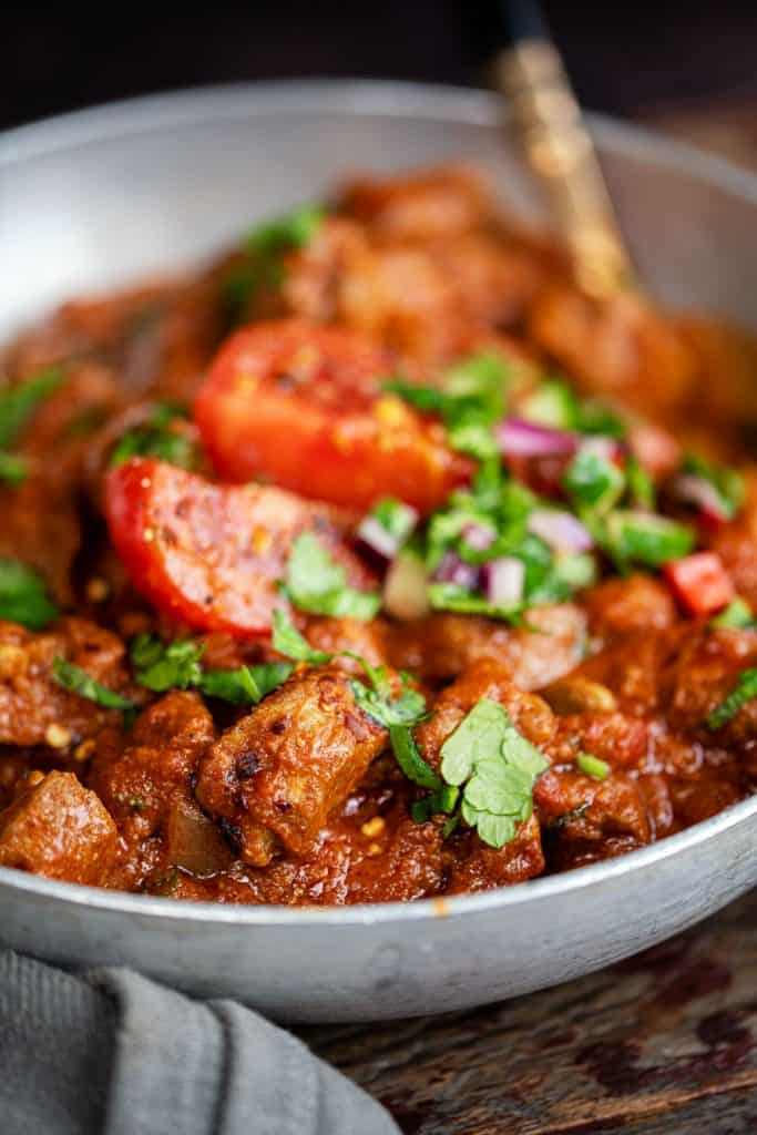 Close up on lamb rogan josh curry garnished with coriander and fresh tomatoes
