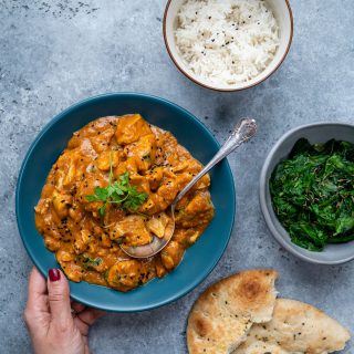Slow cooker chicken curry in a blue bowl with rice on the side and naan bread