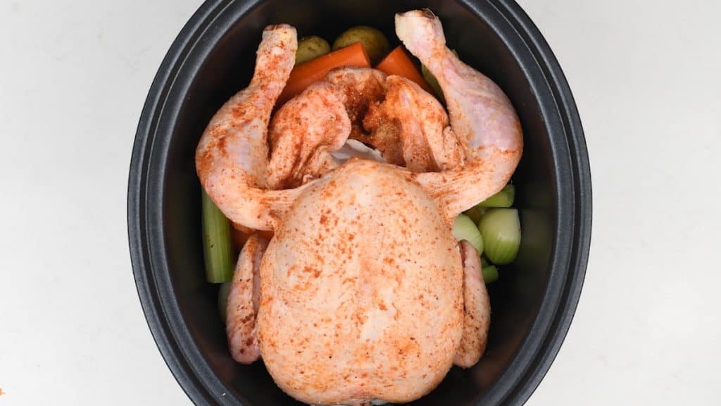 Whole chicken in slow cooker on a bed of vegetables