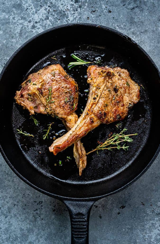 Two pan fried lamb chops in a skillet with rosemary garnish