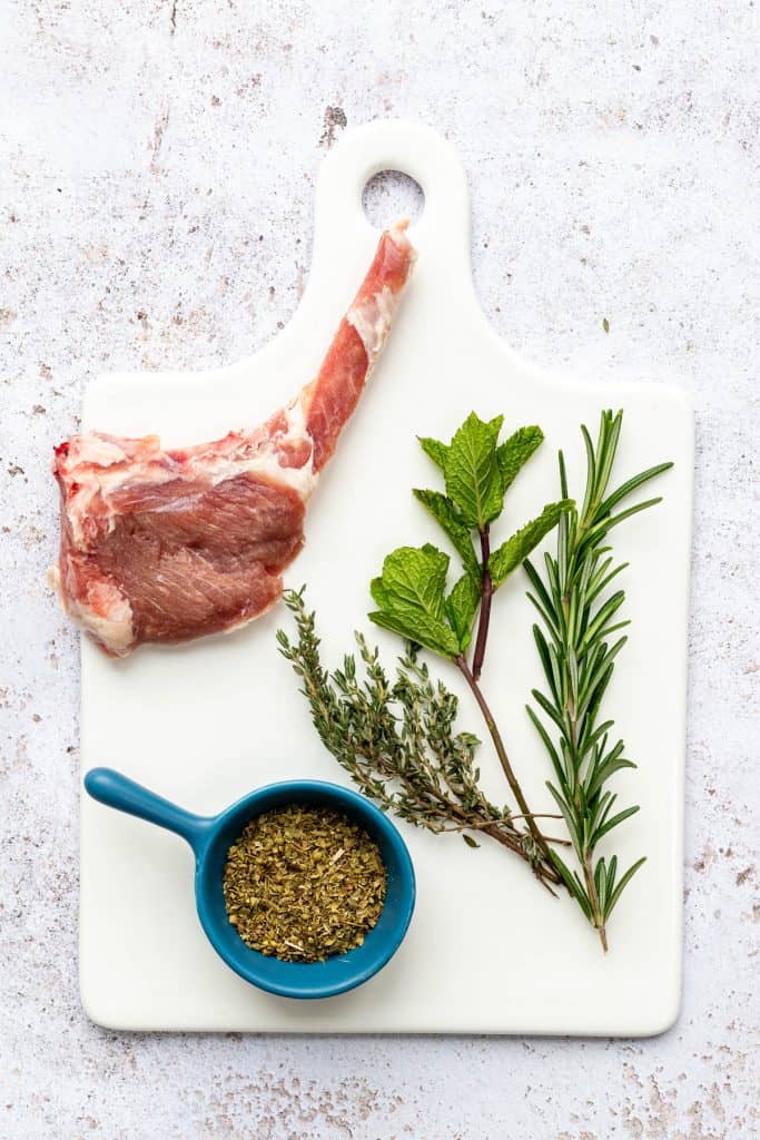 Rosemary, mint, thyme and oregano with a lamb chop on marble board