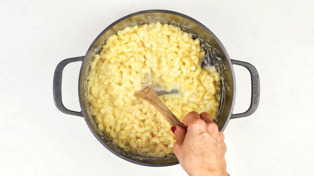 stirring macaroni into cheese sauce in a pot