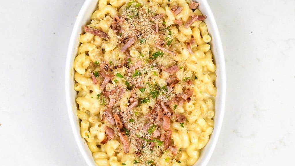 macaroni and cheese in a ceramic dish topped with breadcrumbs and bacon