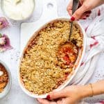 Rhubarb crumble with oat topping in an oval ceramic dish with portion taken out