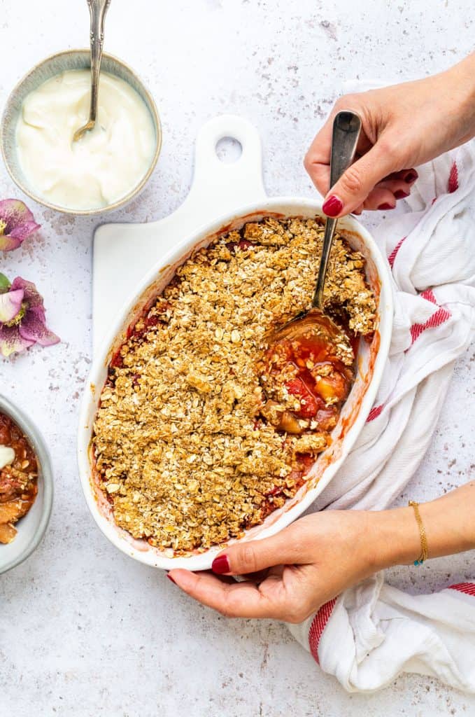 Rhubarb crumble with oat topping in an oval ceramic dish with portion taken out