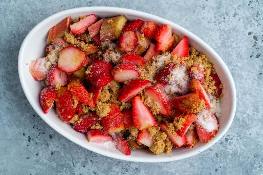 Rhubarb and strawberries tossed with brown sugar in an oval ceramic dish
