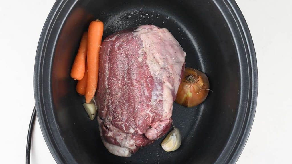 Half leg of lamb in a slow cooker with carrots, onion and garlic
