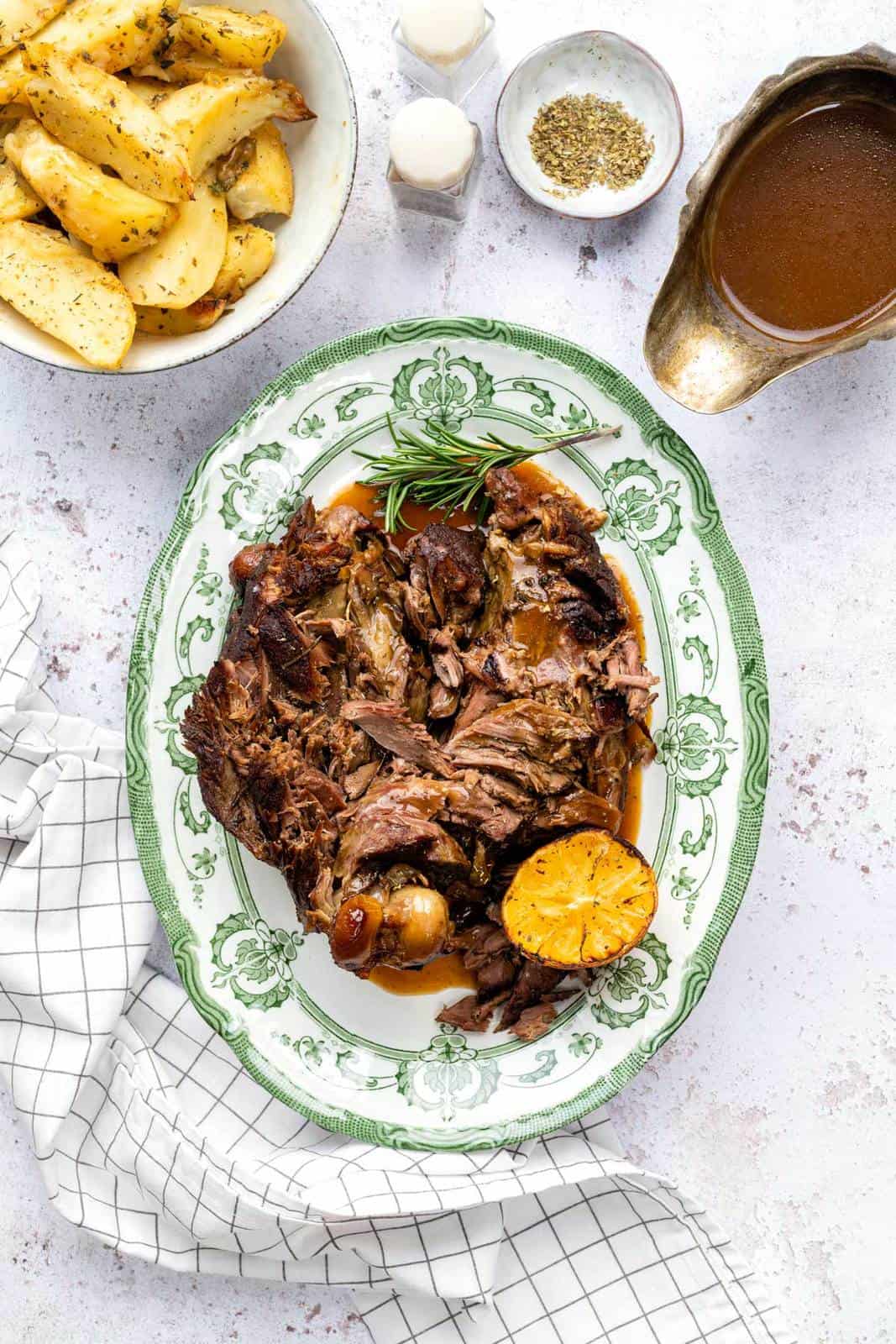 Slow Cooker Roast Lamb, shredded and served on a platter with gravy and roast potatoes on the side