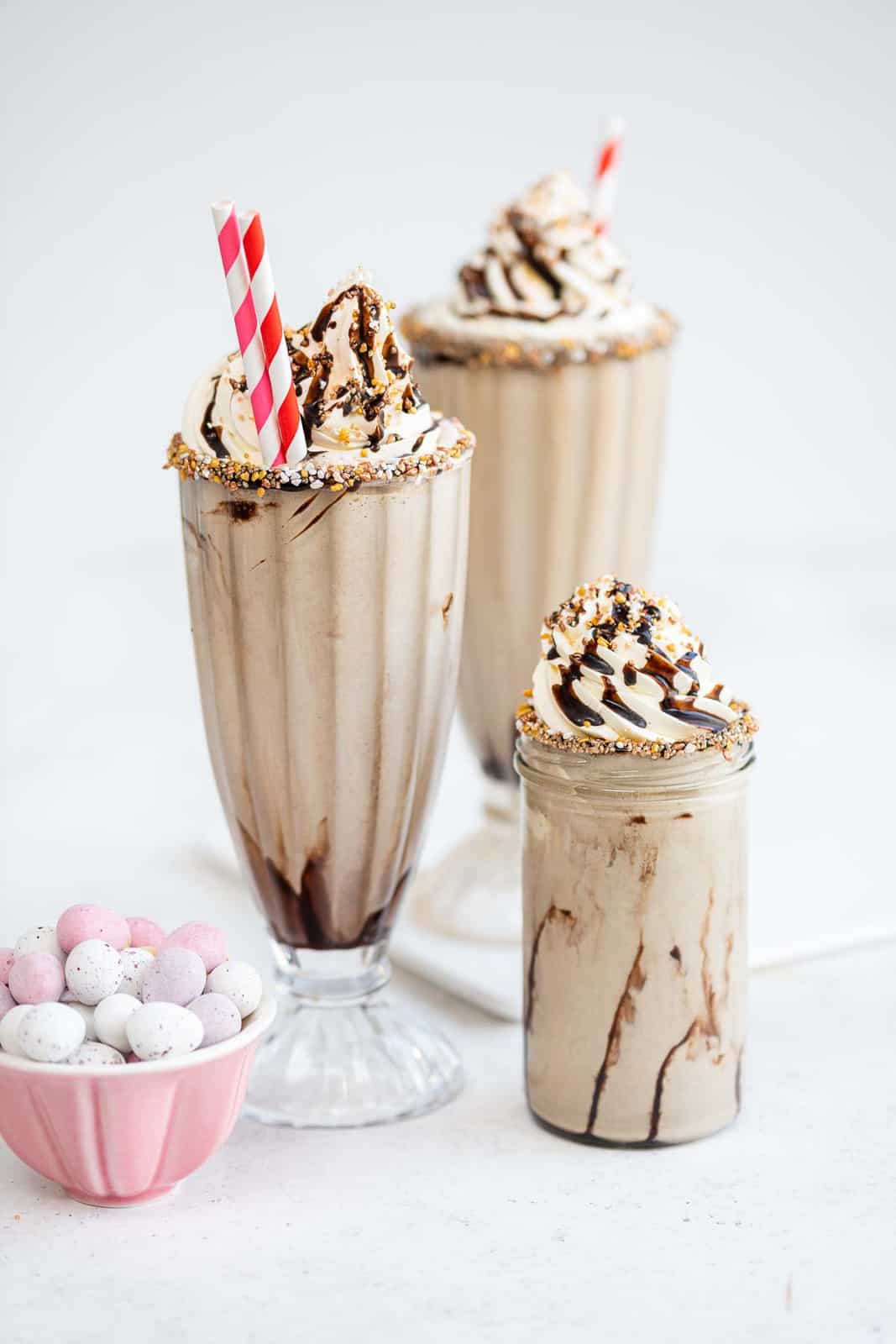 Tree vanilla milkshakes garnished with whipped cream, sprinkles and chocolate sauce