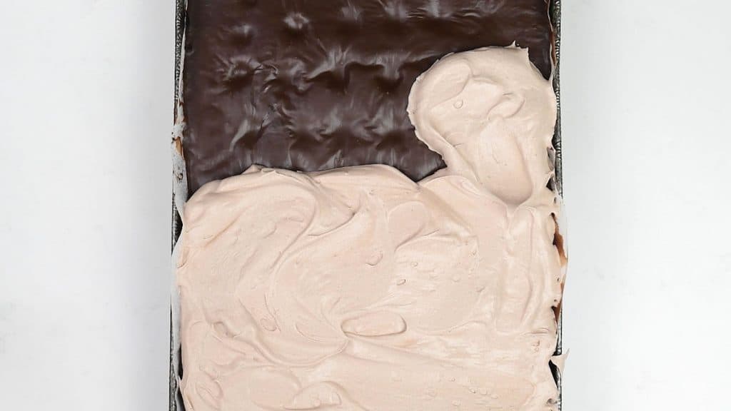 spreading whipped cream frosting over chocolate poke cake