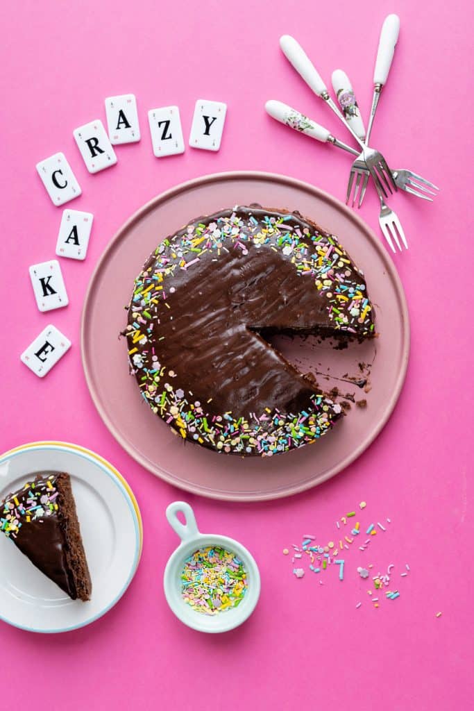 Chocolate wacky cake on a pink plate with slice taken out against pink background