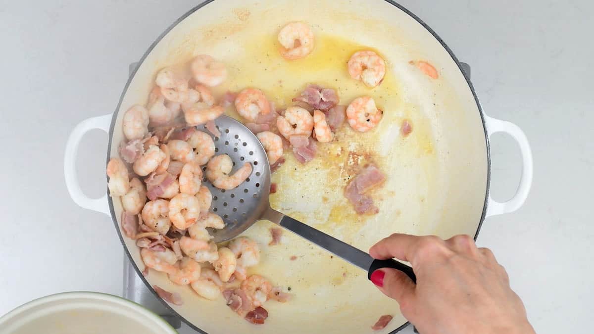transferring shrimp and bacon from a pan into a bowl