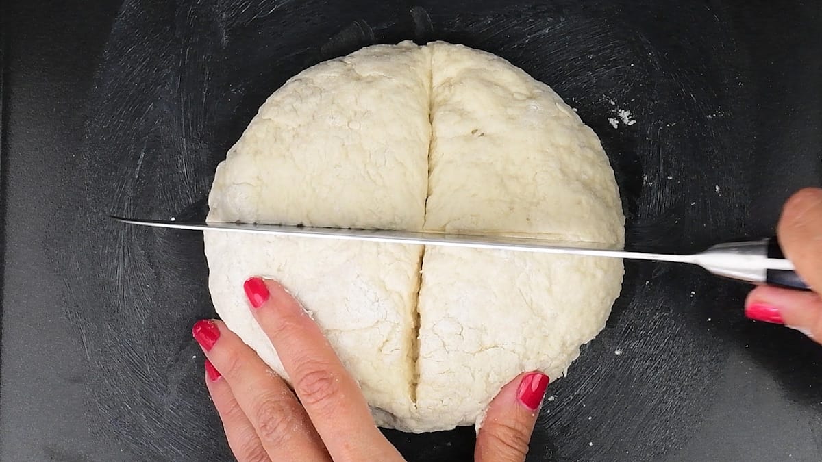 Scoring soda bread loaf with a large knife in a cross shape