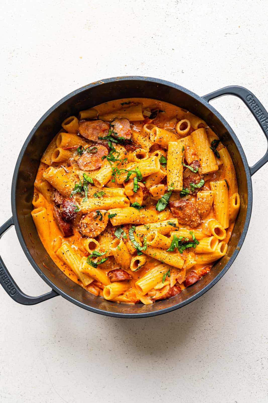 Pot of spicy sausage pasta in tomato and mascarpone sauce garnished with fresh chopped basil