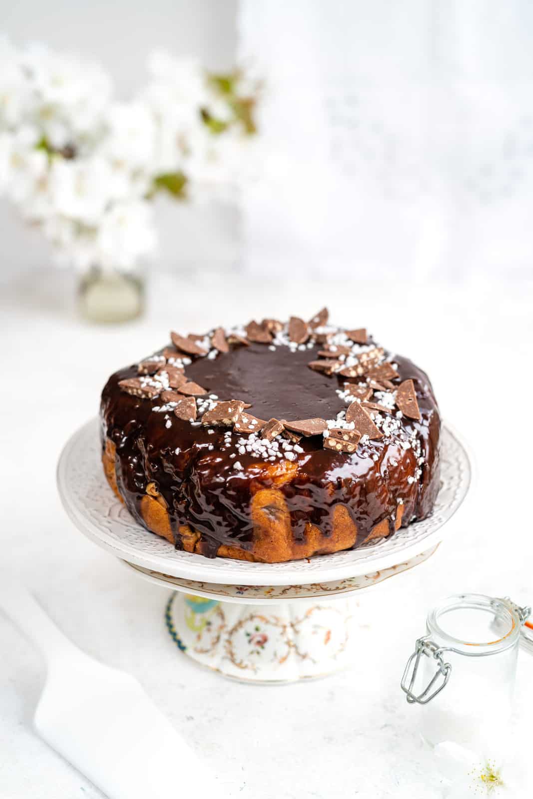 Slow cooker banana bread covered with chocolate glaze and chocolate buttons on a cake stand