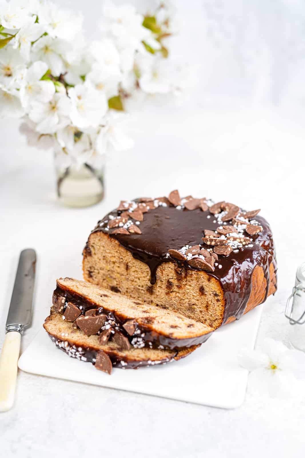 Slow Cooker Banana Bread with chocolate glaze on white ceramic board with slices cut out