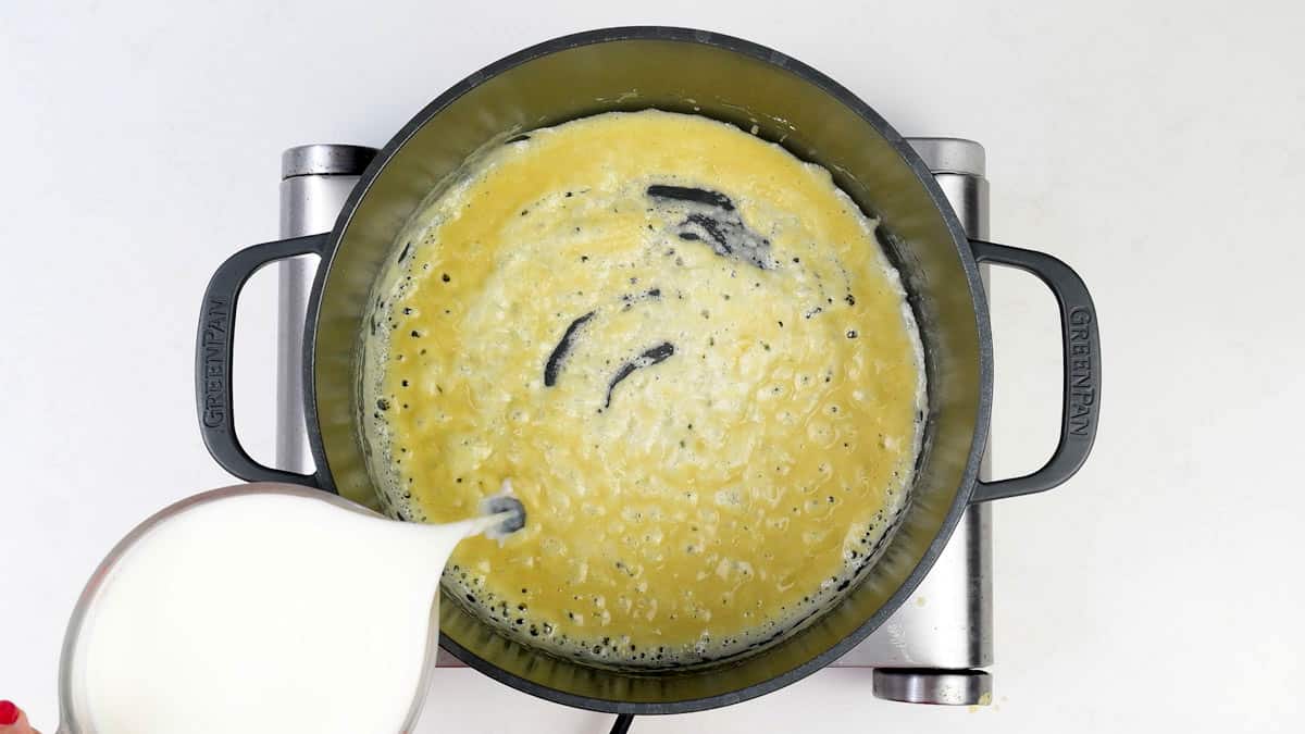 adding milk to roux to make a cheese sauce in a pan