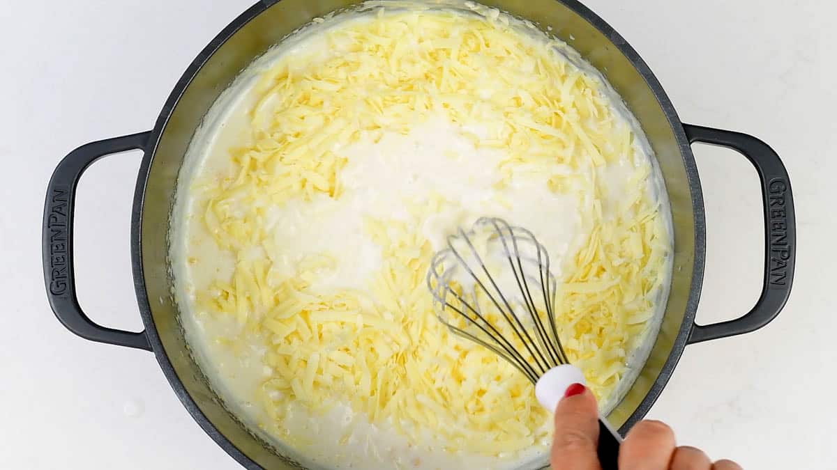 stirring grated cheese into white sauce in a pan