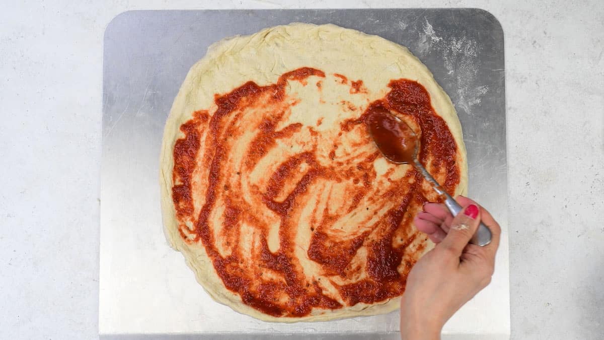 spreading tomato sauce over pizza base