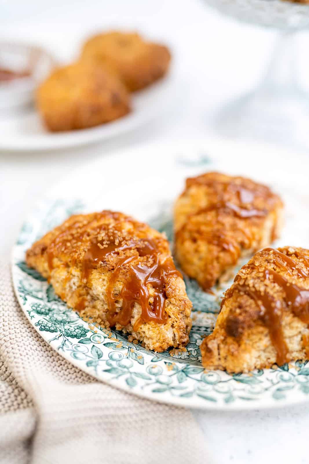 Close up of three apple scones drizzled with caramel on a vintage patterned plate