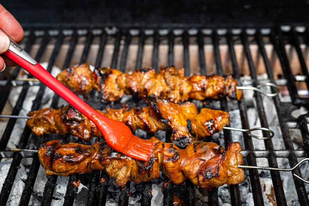 basting lamb skewers with Filipino barbecue sauce on the grill