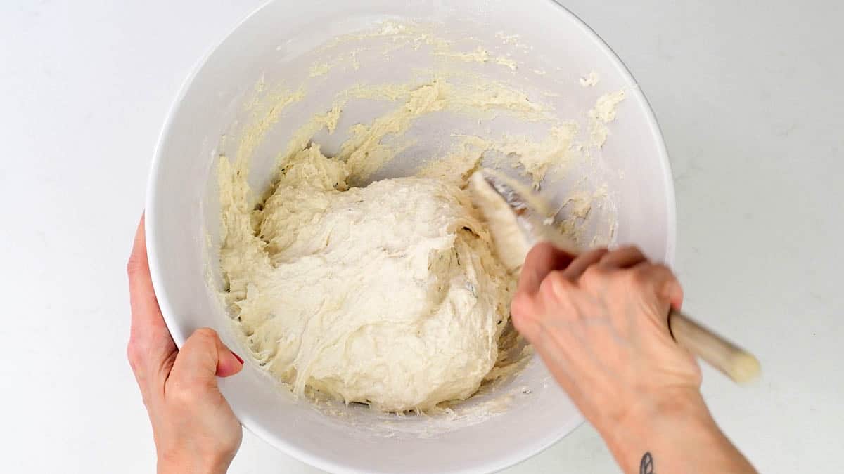 mixing no knead bread dough with a wooden spoon in a mixing bowl