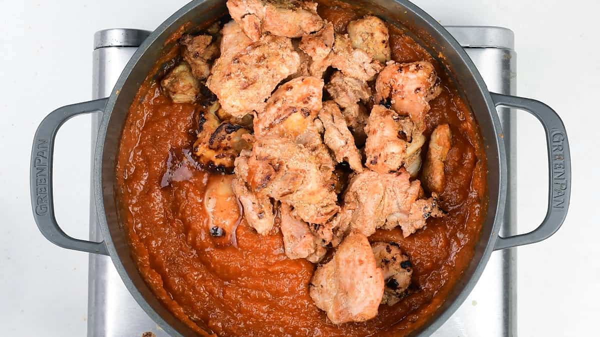 adding grilled chicken into masala sauce in a pot