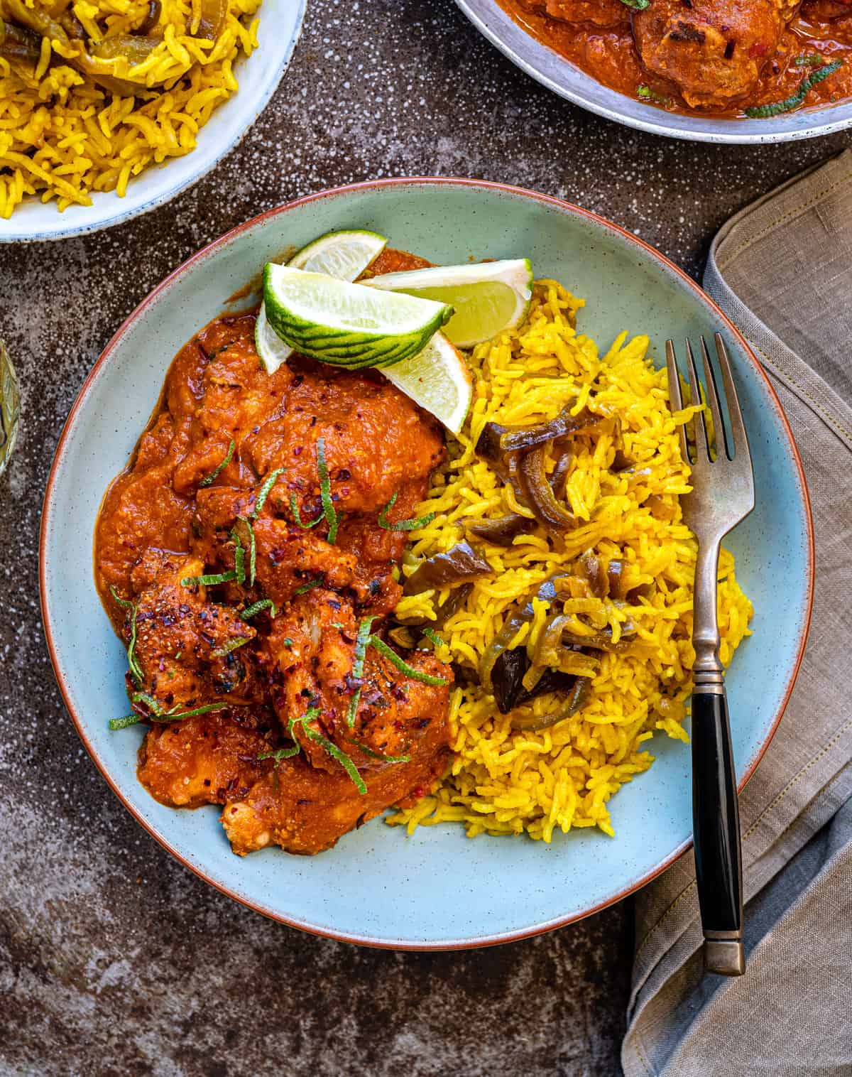 Chicken Tikka Masala served in a bowl with pilau rice and lime wedges on the side