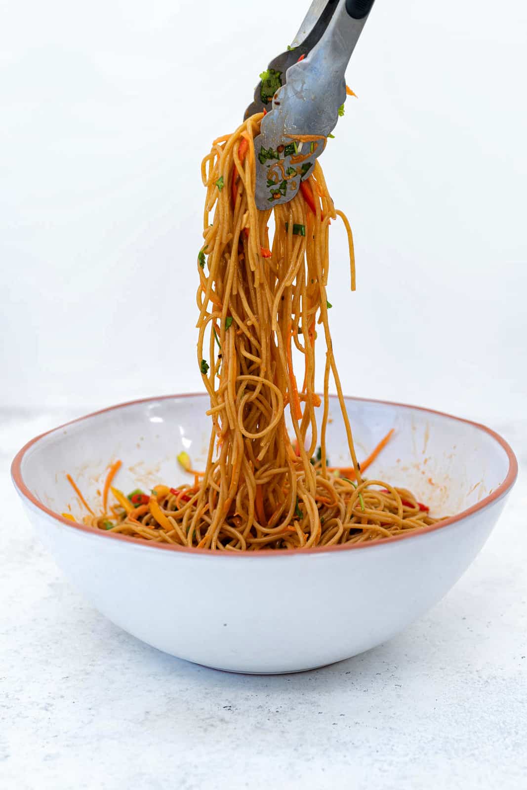 Tossing noodles with spicy peanut sauce and vegetables in a bowl