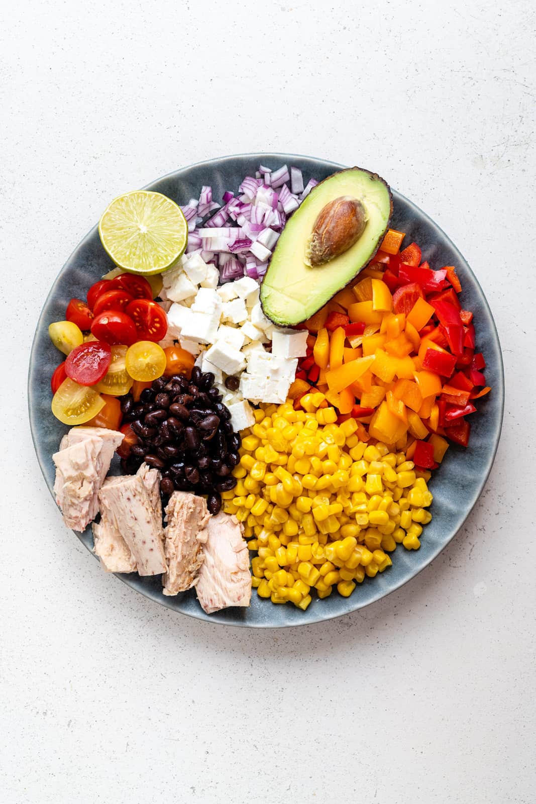 Plate with diced peppers, corn, tuna, black beans, tomatoes, feta cheese, onion and avocado