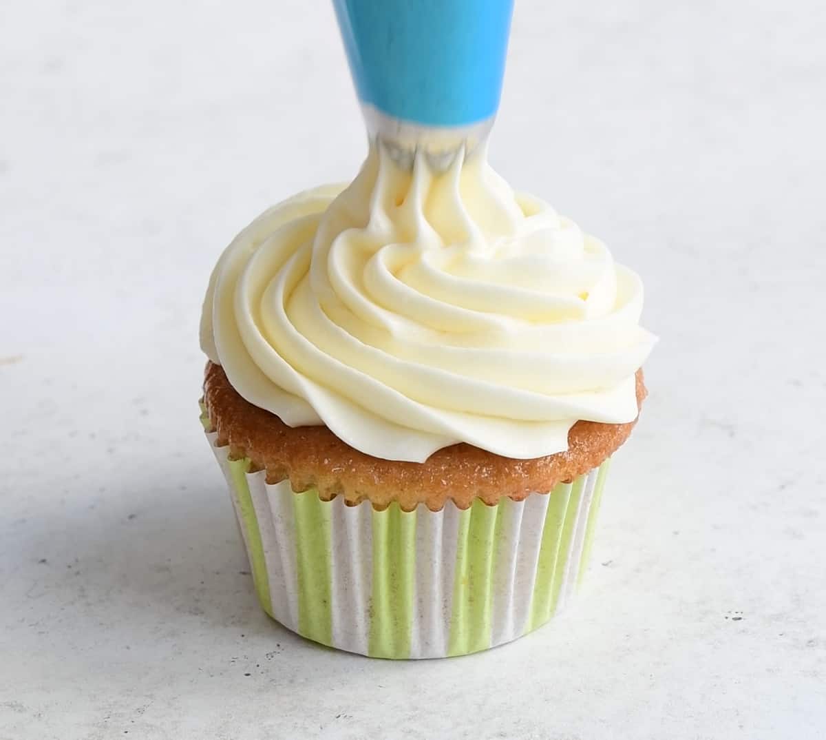 piping cream cheese frosting over lemon cupcakes