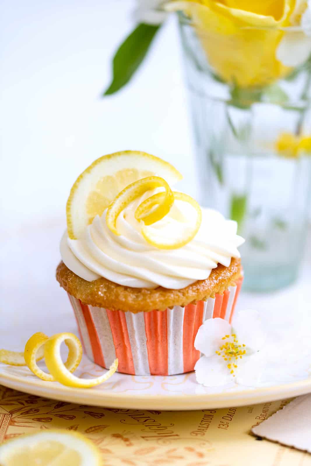 lemon drizzle cupcake topped with cream cheese frosting and garnished with lemon zest and slice on a plate