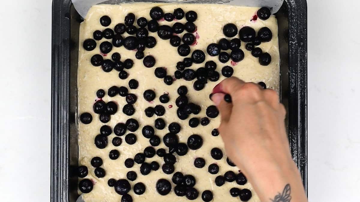 spreading blueberries over cake batter in a square tin