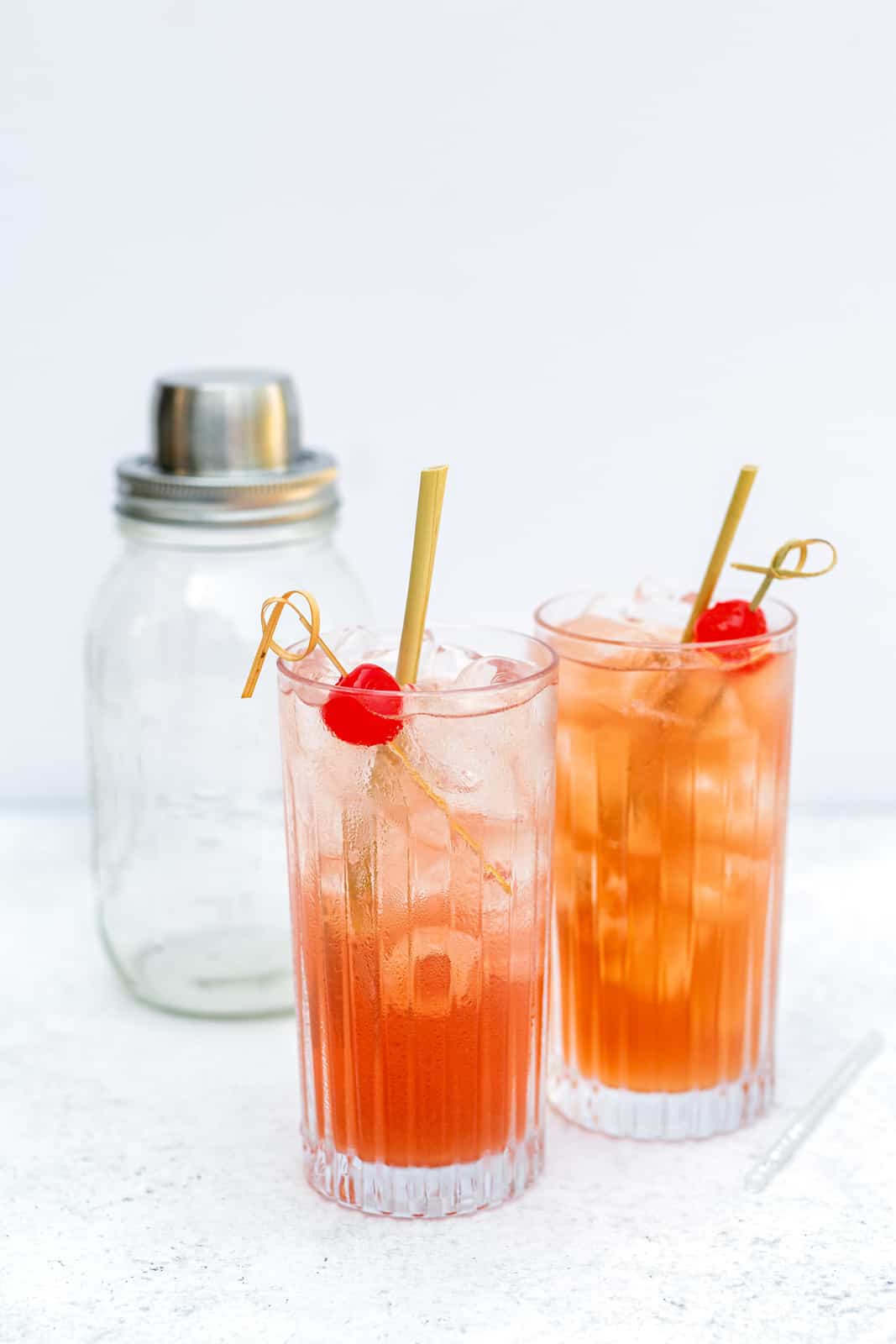 Singapore Sling served in two tall glasses filled with ice, garnished with cocktail cherries and straws